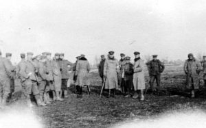 A dozen men in winter military wear stand around, their conversations paused to turn towards the camera.
