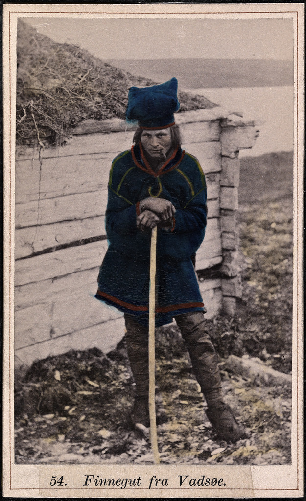 a 1900s Norwegian fisherman in a sturdy square deep blue sweater/coat/dress and a strange puffy-topped hat (looks kind of like a chef's hat), also colored with the same striking blue. Resting on a staff with a pipe in his mouth, head bent slightly down but eyes beaming up and out.